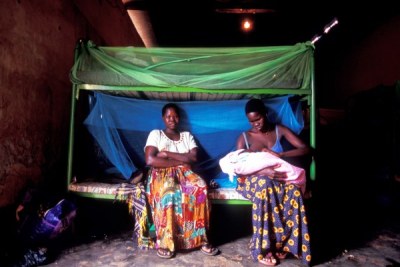 Two former abducted girls sit on a bed under the mosquito net.