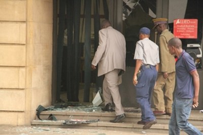 Police officers assess the damage on the glass door and windows at Allied Bank in Harare.