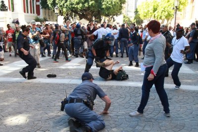 A police officer attempts to apprehend a protesting UCT student near Parliament as others look on.