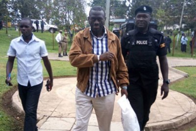 A policeman leads Dr Besigye to court.