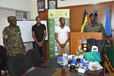 Gashumba (white T-shirt) paraded in front of the press. On the desk are several items like stamps and passports that the army said were used to pursue fraudulent activities.