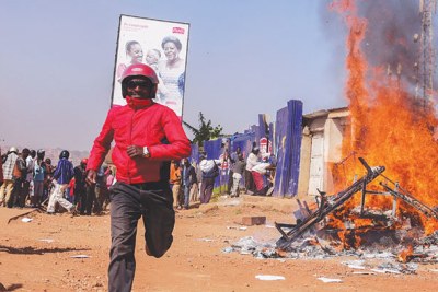 A boda-boda rider flees from the burning Boda Boda 2010 offices in Nateete on Monday.